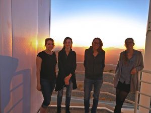 Bethany Ludwig, Anna O’Grady, Maria Drout and Ylva Götberg stand on a deck at the Magellan telescopes in front of a sunset.